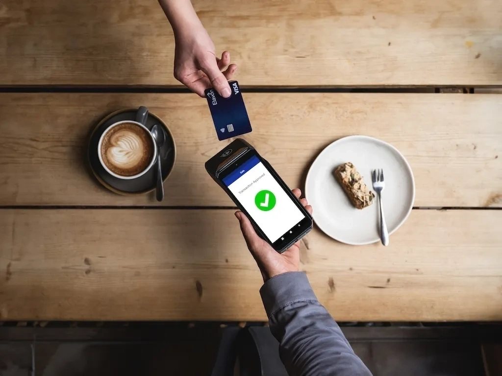 Customer making a contactless card payment using an Elavon payment terminal at a café table
