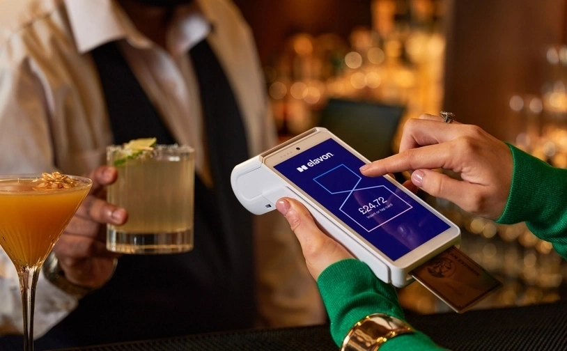 Contactless card payment at a bar using a handheld POS terminal while bartender serves cocktails