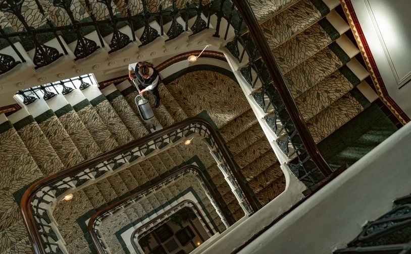 Person standing on a patterned stairwell, viewed from above through multiple spiral landings.