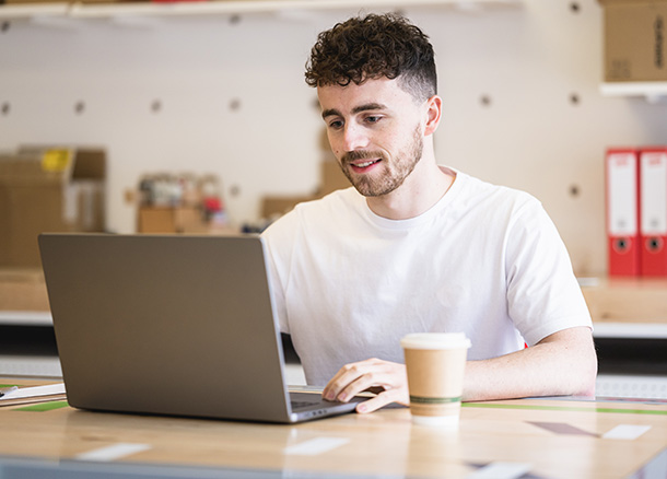 A person sitting at a desk working on a laptop with a coffee cup on desk